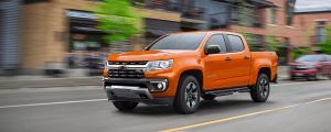 Orange Chevrolet Colorado zooming down a city street.