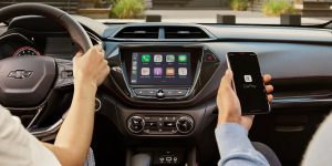 Close up photo of two people, one is driving and one is holding their phone displaying that it is connected to Apple Car Play in their Chevrolet Trailblazer.