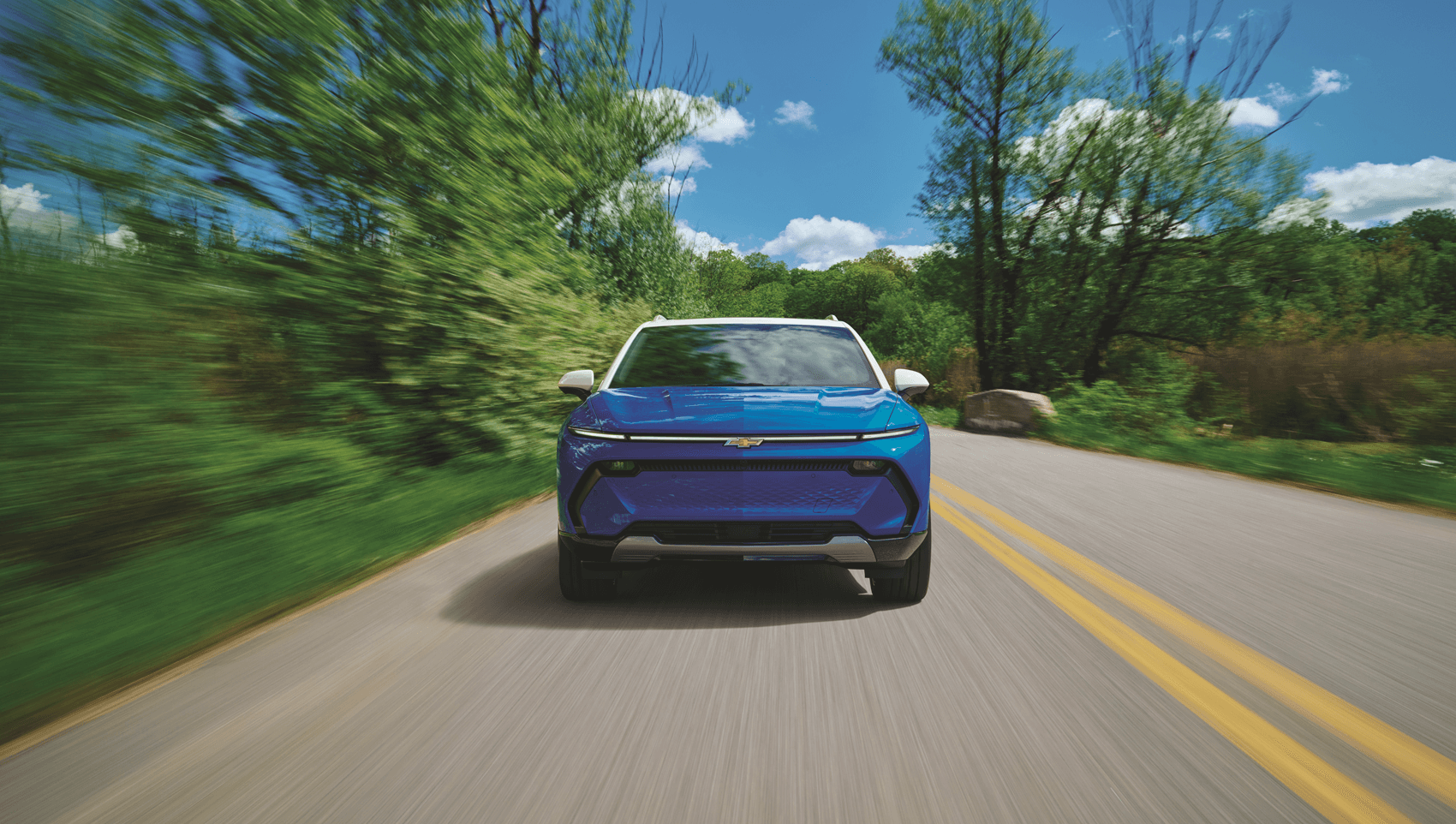 Blue Chevrolet Equinox EV Diving on road with trees